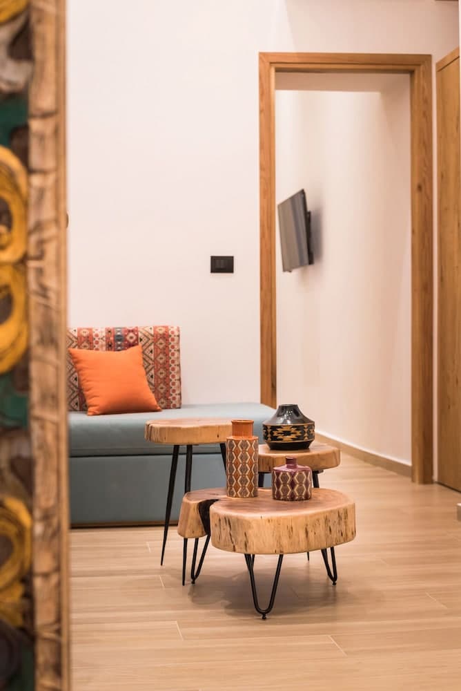 A cozy living room features a vibrant orange pillow on a patterned sofa, rustic wooden tables adorned with decorative vases, and a minimalist ambiance ideal for travelers seeking a serene and stylish accommodation.