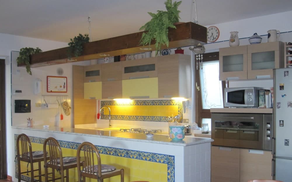 A cozy kitchen with yellow-tiled walls, wooden beams adorned with greenery, and a bar counter with stools invites travelers to enjoy a warm, homey atmosphere perfect for culinary adventures.