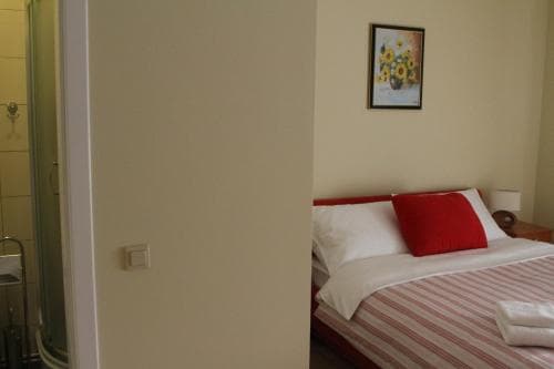 A cozy hotel room features a neatly made bed with red accents, a sunflower painting on the wall, and an adjacent bathroom, ideal for travelers seeking comfort and simplicity.