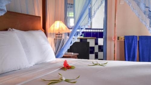 A cozy bedroom with a neatly made bed adorned with tropical flowers, blue curtains, and soft lighting creates a serene atmosphere ideal for relaxation during a tropical getaway.