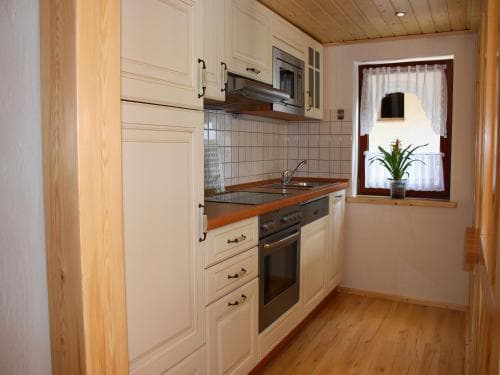 A cozy, well-lit kitchen with white cabinetry, wooden flooring, and a window adorned with a potted plant creates a warm and inviting atmosphere ideal for travelers seeking a homey rental experience.