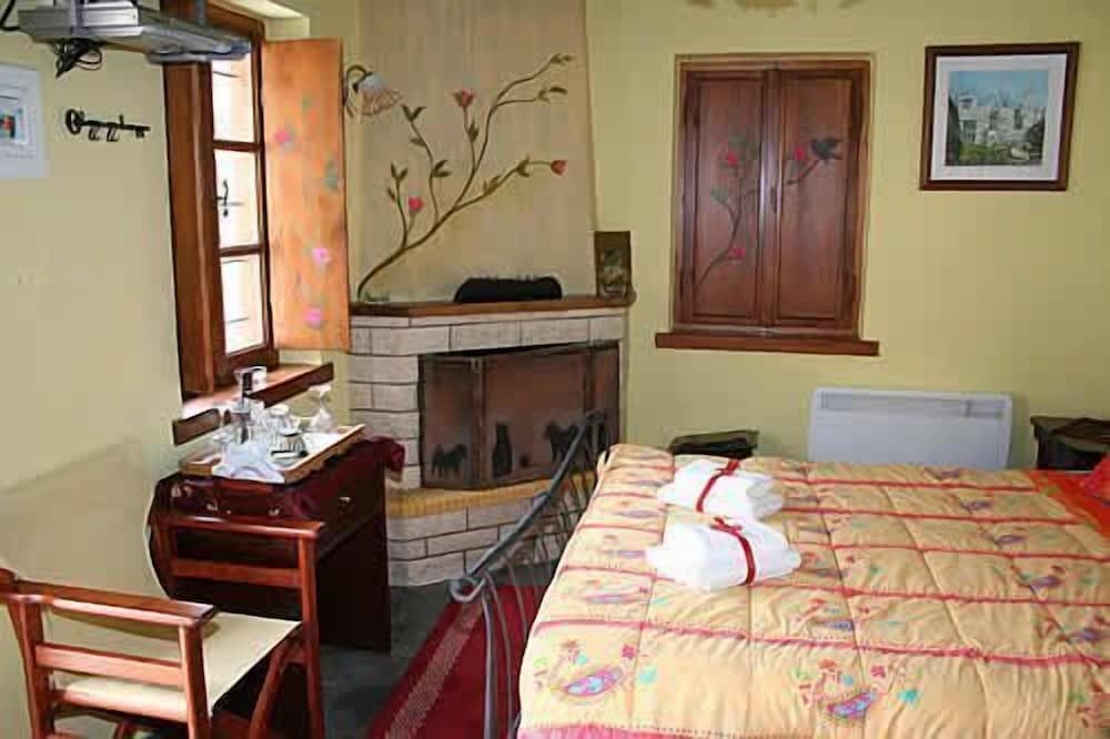 A cozy bedroom with a floral-patterned bedspread, wooden furniture, and a fireplace adorned with painted flowers offers a warm and inviting atmosphere ideal for travelers seeking a quaint and comfortable stay.