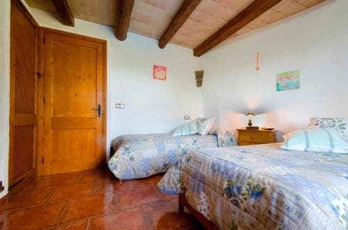 A cozy bedroom with rustic wooden beams, terracotta flooring, and floral bedding offers a serene retreat ideal for travelers seeking a tranquil countryside stay.