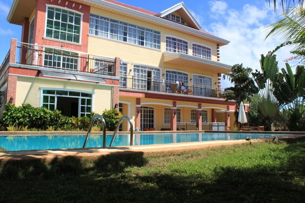 A vibrant, two-story villa with balconies overlooks a serene pool surrounded by lush tropical greenery, ideal for a relaxing vacation retreat.