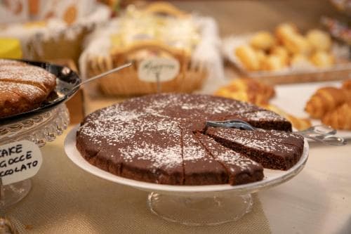 A delightful bakery display features a rich chocolate cake dusted with powdered sugar on a glass stand, surrounded by assorted pastries, evoking a cozy and inviting atmosphere perfect for a sweet indulgence during a leisurely café visit.