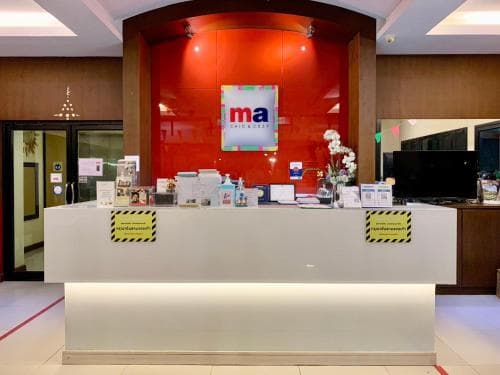 A modern hotel reception area features a sleek white desk adorned with safety signs, a vibrant red backdrop, and a welcoming ambiance ideal for travelers seeking comfort and convenience.