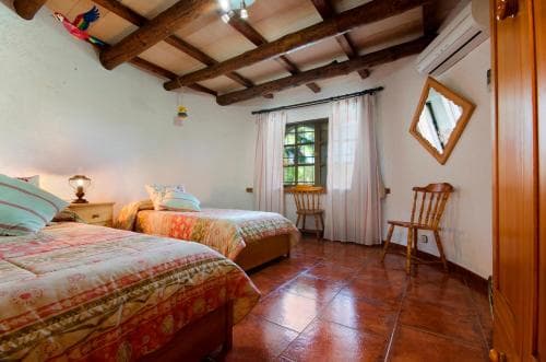 A cozy rustic bedroom with wooden beams, terracotta tiled floors, and twin beds adorned with colorful linens invites travelers seeking a charming countryside retreat.