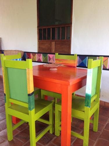 A vibrant outdoor dining area features colorful wooden chairs and a table set against a rustic wall, creating a cheerful and inviting atmosphere perfect for family gatherings or casual dining experiences.