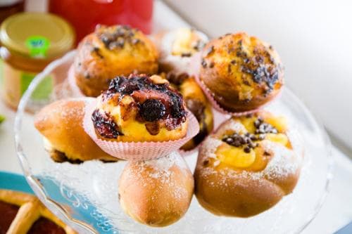 A cozy café scene features a glass platter of assorted pastries, including cream-filled buns and berry-topped muffins, creating an inviting atmosphere perfect for a leisurely breakfast or brunch outing.