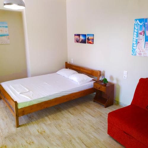 A cozy hostel room features a wooden bed, red sofa, and vibrant wall art, creating a welcoming atmosphere ideal for budget travelers seeking comfort.