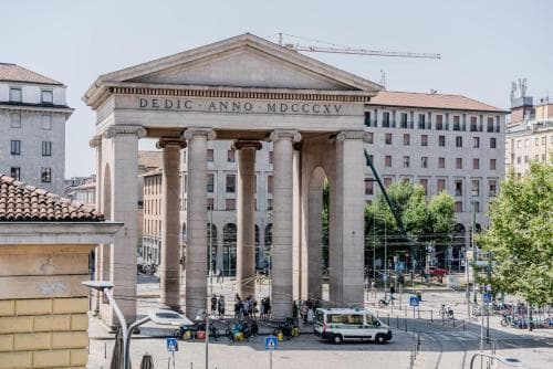 A grand neoclassical temple with prominent columns stands in an urban square, surrounded by modern buildings and bustling activity, ideal for cultural exploration and architectural appreciation.