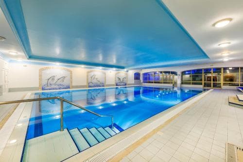 A serene indoor swimming pool with blue-tiled walls, artistic murals, and modern lighting offers a tranquil retreat for relaxation and fitness enthusiasts.
