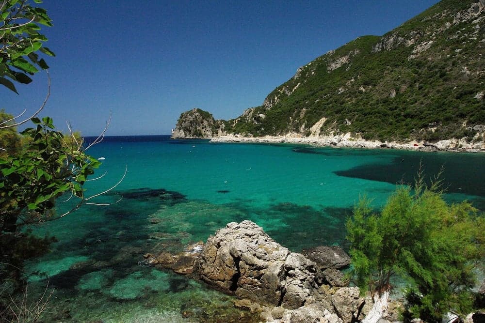 A serene coastal cove framed by lush green hills and turquoise waters, ideal for tranquil beachside relaxation and nature photography.