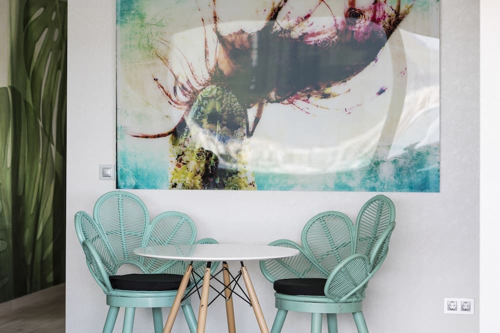 A cozy café corner features teal wicker chairs around a small white table beneath a vibrant floral artwork, creating an inviting atmosphere perfect for travelers seeking a relaxing spot to unwind.