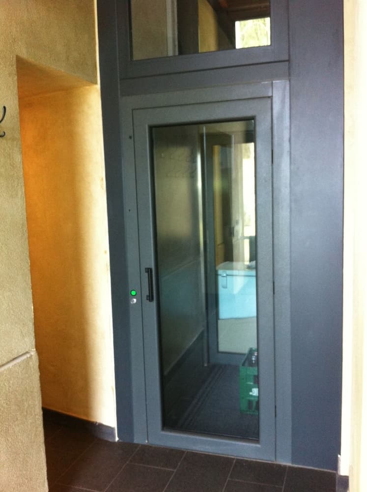 A modern glass door framed in dark metal opens into a warmly lit interior hallway, ideal for showcasing architectural design elements in a residential or commercial property tour.