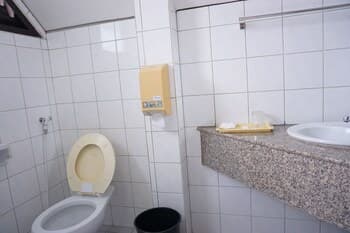 A clean, tiled restroom with a toilet, sink, soap dispenser, and trash bin offers a functional space for travelers needing basic facilities during their journey.