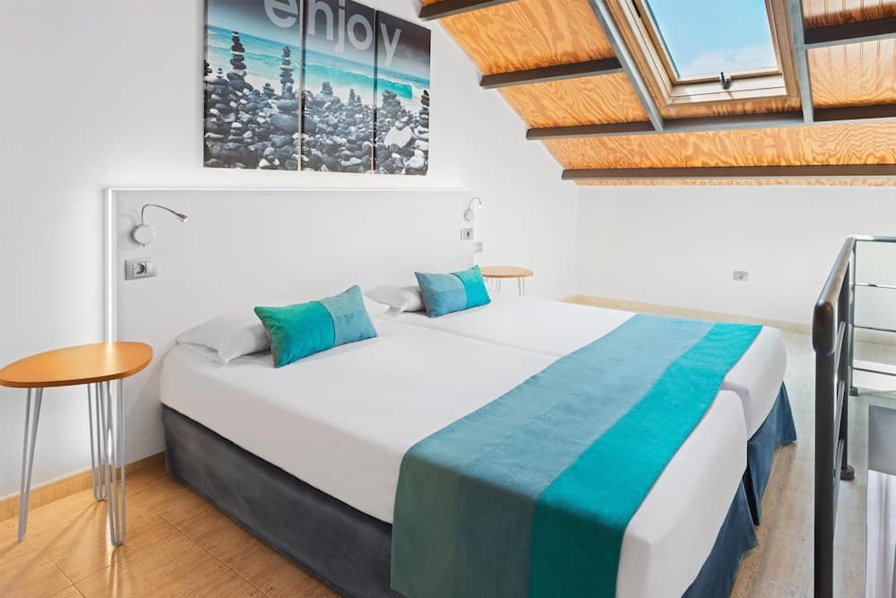 A cozy attic bedroom with a sloped wooden ceiling, skylight, and vibrant blue accents creates a serene retreat, ideal for travelers seeking a peaceful stay in a modern vacation rental.