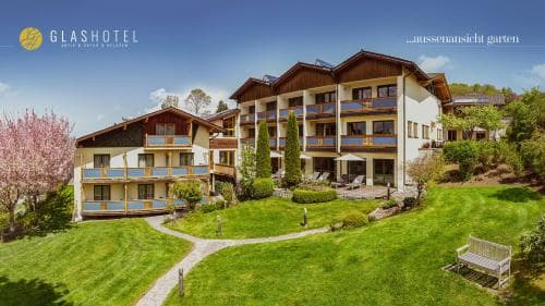 A serene alpine hotel with lush green lawns, blooming trees, and cozy balconies offers a tranquil retreat for travelers seeking relaxation in nature.