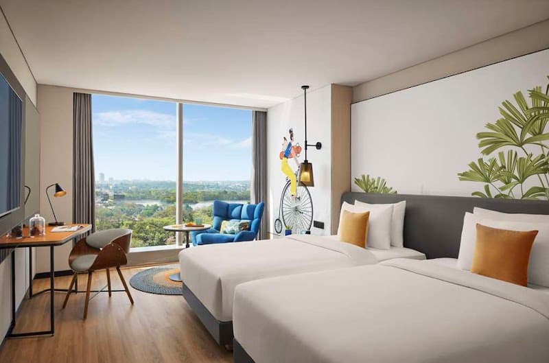 A cozy hotel room at Hyatt Centric Hebbal Bengaluru features modern decor, twin beds with vibrant pillows, a scenic city view through large windows, and a playful wall art piece, ideal for travelers seeking comfort and style in Karnataka, India.