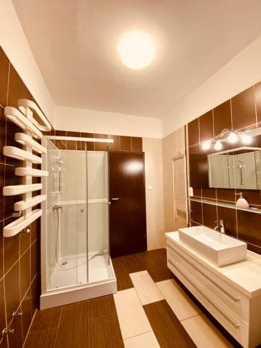 A modern bathroom with sleek wooden flooring, a glass-enclosed shower, a floating vanity with a vessel sink, and a wall-mounted towel warmer creates a cozy and luxurious atmosphere, ideal for travelers seeking comfort in upscale accommodations.