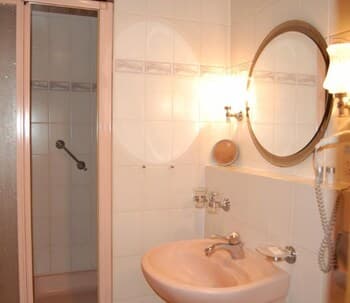 A cozy hotel bathroom features a tiled shower, sink, and round mirror under warm lighting, ideal for travelers seeking comfort and cleanliness.