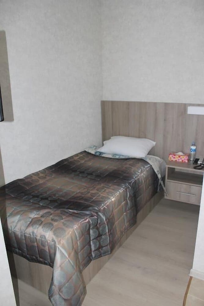 A cozy hotel room features a neatly made bed with a patterned quilt, a wooden bedside table holding personal items, and light-colored walls, ideal for travelers seeking comfort and simplicity.