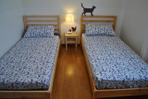 A cozy bedroom with two wooden beds adorned in blue floral bedding, a small bedside table with a lamp, and playful cat decals on the wall, ideal for travelers seeking a comfortable and charming accommodation.