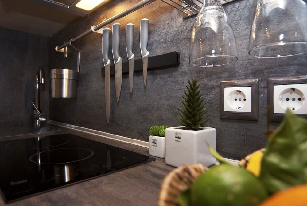 A cozy kitchen corner features sleek knives on a magnetic strip, hanging wine glasses, and vibrant plants, creating an inviting atmosphere ideal for culinary enthusiasts exploring modern home cooking setups.