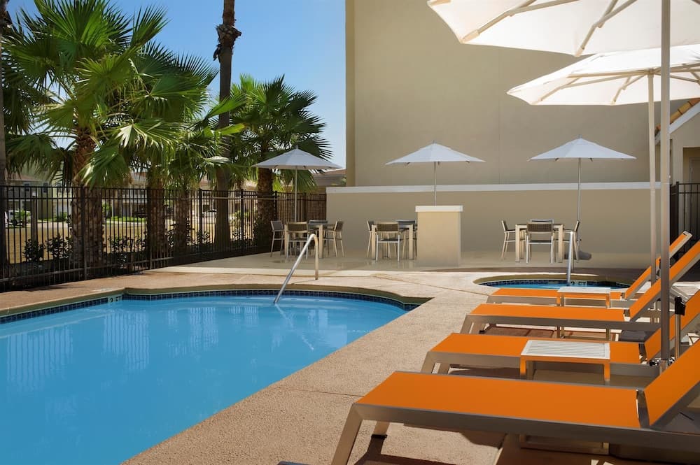 A serene hotel poolside scene features vibrant orange lounge chairs under white umbrellas, surrounded by lush palm trees, ideal for relaxing vacations or leisurely getaways.