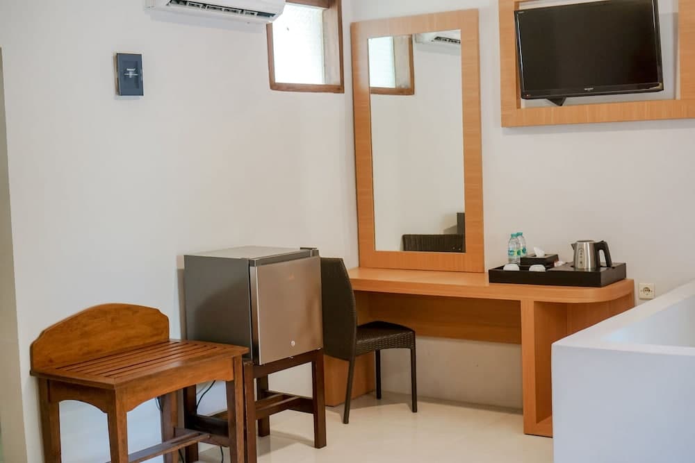 A cozy hotel room corner features a wooden desk with a mirror, a mini-fridge, a kettle set, and a flat-screen TV, creating a functional and inviting space for travelers seeking comfort and convenience.