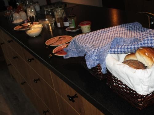A cozy kitchen countertop scene featuring a basket of fresh bread under a blue checkered cloth, alongside plates of food and jars, evokes a warm, homely atmosphere perfect for culinary enthusiasts exploring local dining experiences.