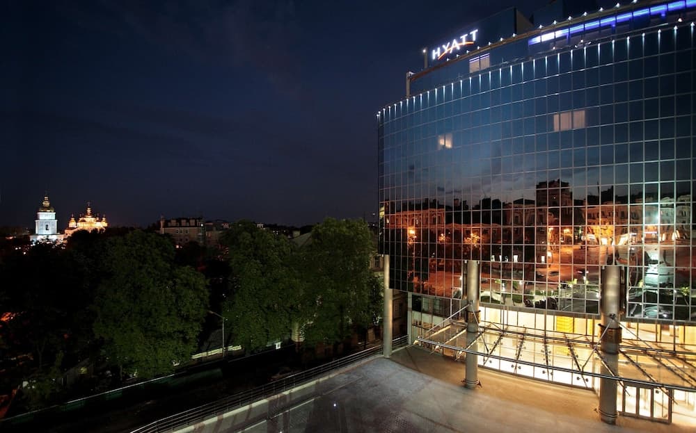 A modern Hyatt hotel with illuminated glass panels stands against the night sky, overlooking a serene urban landscape with historic domed buildings, ideal for travelers seeking luxury accommodations in a vibrant city setting.
