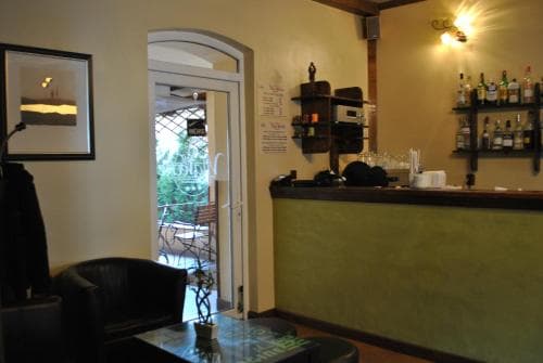 A cozy indoor café scene features a warmly lit bar area with neatly arranged bottles, comfortable seating, and an inviting doorway leading to a patio, perfect for travelers seeking a relaxing spot for refreshments.