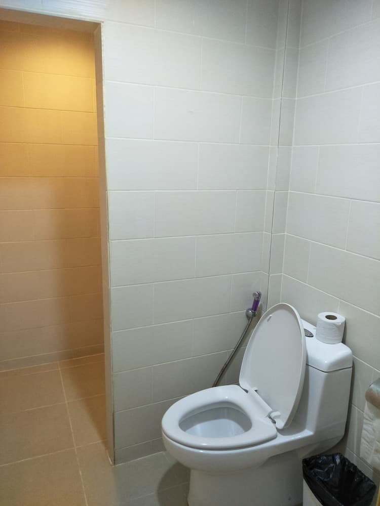 A clean, tiled bathroom features a white toilet with an open lid, a purple bidet sprayer, and a roll of toilet paper on the tank, ideal for travelers seeking basic restroom facilities.
