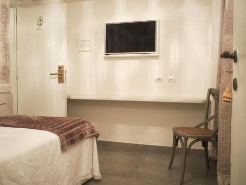 A cozy hotel room features a neatly made bed, a rustic chair, and a wall-mounted TV, creating a serene atmosphere ideal for travelers seeking relaxation.