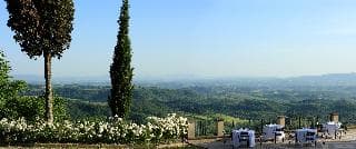 A serene hilltop vista overlooking lush green valleys, framed by blooming white flowers and tall cypress trees, evokes a tranquil mood ideal for relaxation and scenic photography.