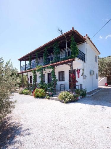 A charming two-story villa with a red-tiled roof and lush greenery exudes a serene Mediterranean vibe, perfect for a tranquil vacation retreat.