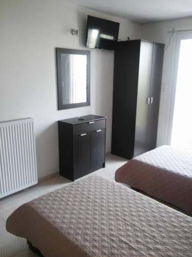 A cozy hotel room features two neatly made beds, modern black furniture, a wall-mounted TV, and natural light streaming through a window, ideal for travelers seeking comfort and simplicity.