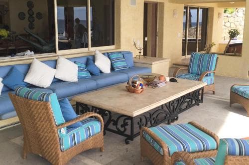 A cozy outdoor patio features comfortable striped furniture and a rustic coffee table, set against a backdrop of large windows and warm-toned walls, ideal for relaxing retreats or vacation rentals.