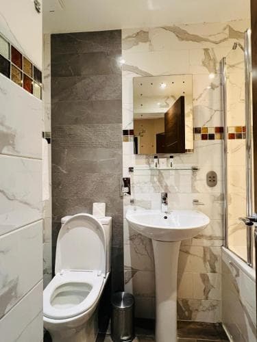 A modern bathroom with marble tiles, a sleek pedestal sink, and a glass shower enclosure offers a clean and stylish space ideal for travelers seeking comfort in accommodations.