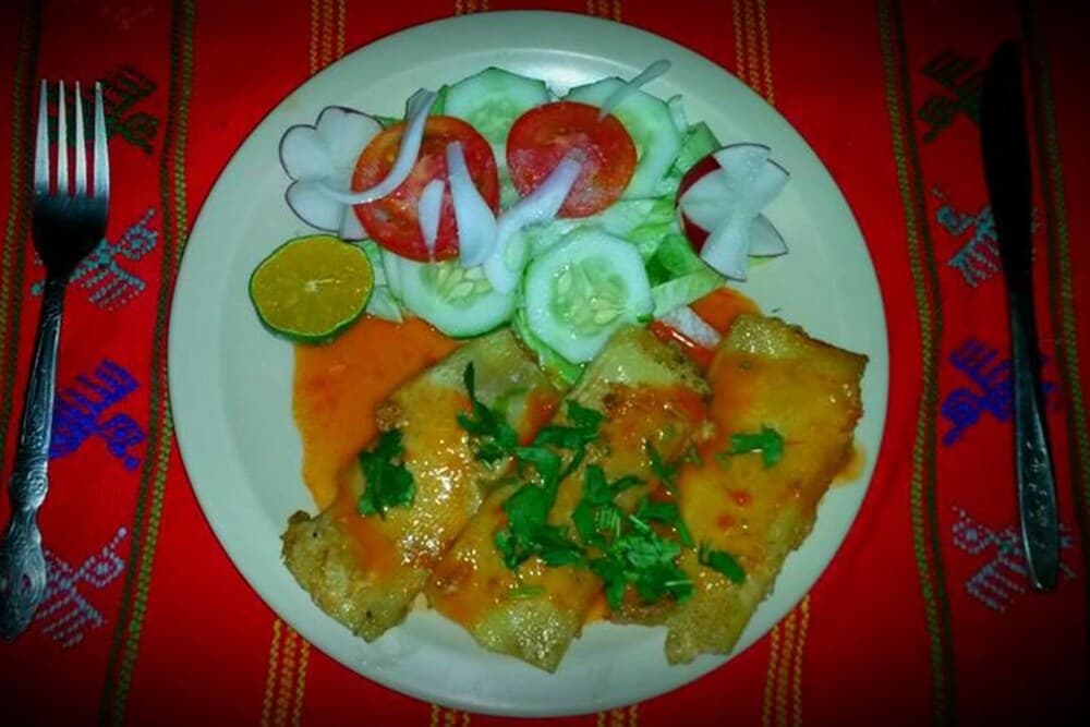 A vibrant plate of savory dumplings garnished with fresh herbs and a side salad sits invitingly on a richly patterned red tablecloth, perfect for travelers seeking authentic local cuisine in a cozy dining setting.