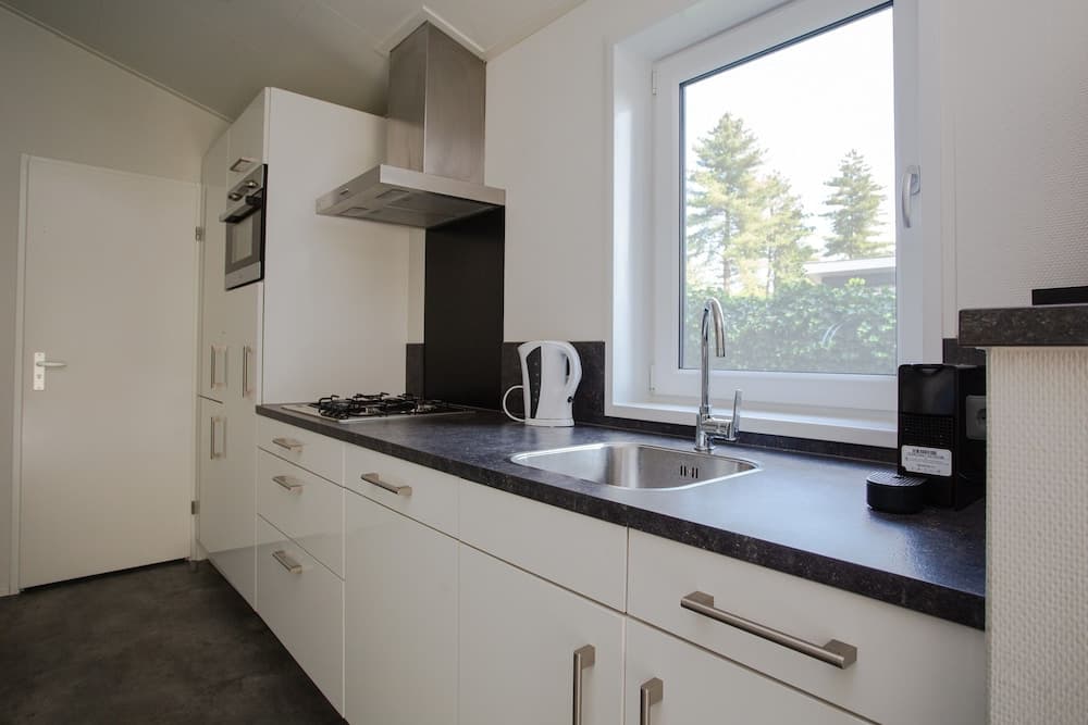 A modern, minimalist kitchen with white cabinets, a sleek black countertop, and a bright window offering a serene view of greenery, ideal for travelers seeking a cozy self-catering accommodation.