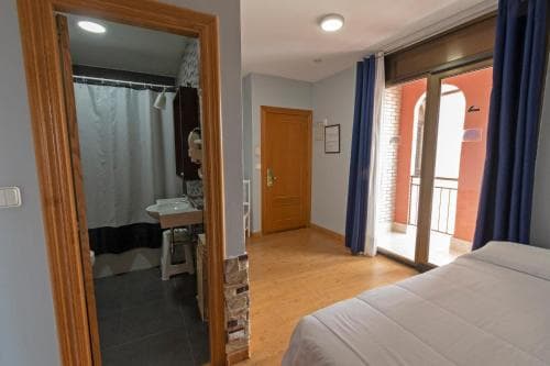 A cozy hotel room with wooden floors, a neatly made bed, and a view of a balcony with red walls, ideal for travelers seeking comfort and convenience.