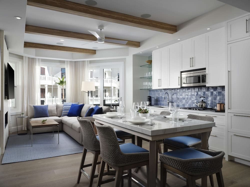 A cozy open-concept living and dining area with white cabinetry, blue accents, and large windows offers a serene retreat ideal for vacation rentals or home staging.