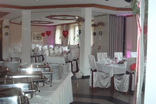 A cozy banquet hall adorned with heart decorations and white tablecloths creates an intimate atmosphere ideal for romantic gatherings or small celebrations, featuring a buffet setup ready for guests.