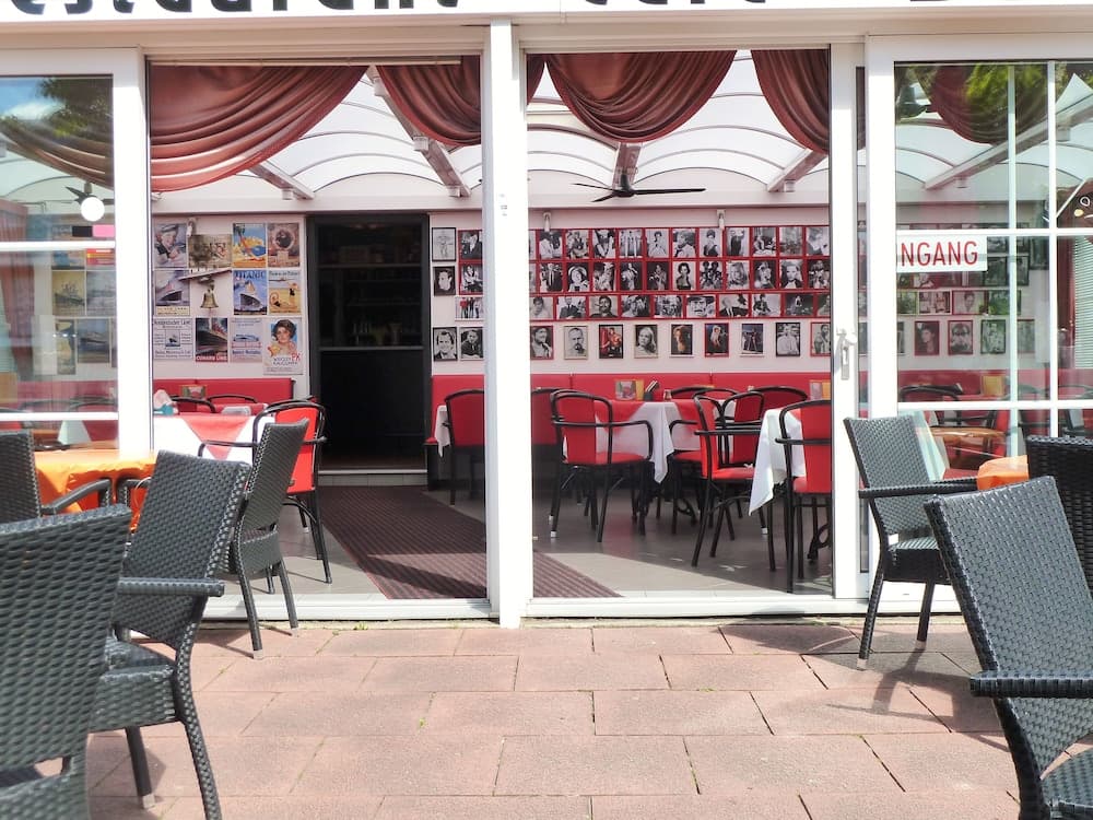 A cozy café with vibrant red interiors, wall-mounted photographs, and outdoor seating invites travelers to relax and enjoy a leisurely meal in a charming urban setting.