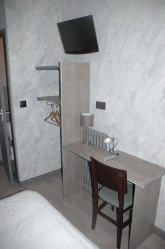A cozy hotel room features a sleek desk setup with a chair, lamp, and mounted TV against textured walls, ideal for travelers seeking a functional yet minimalist space for work or relaxation.