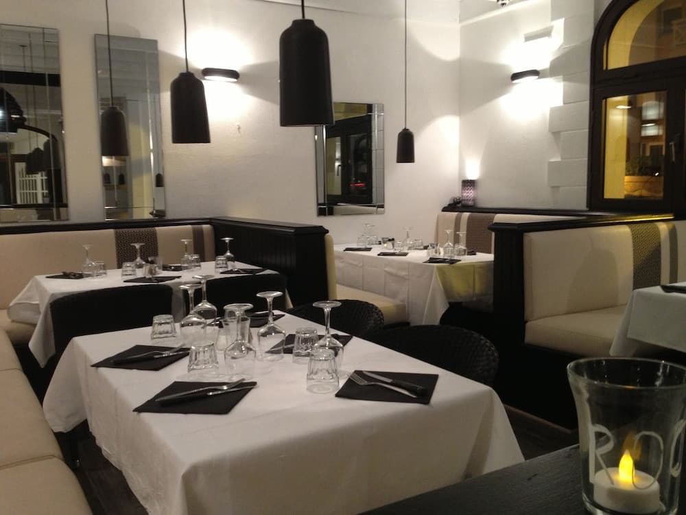 A cozy restaurant interior features neatly set tables with white linens, black pendant lights, and soft lighting, creating an inviting ambiance ideal for romantic dinners or intimate gatherings.