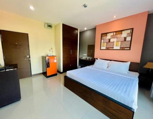 A cozy hotel room features a neatly made bed, vibrant orange accents, and modern furnishings, ideal for travelers seeking comfort and convenience during their stay.