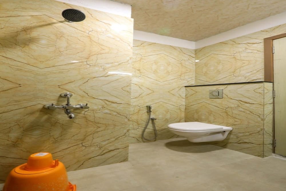 A luxurious bathroom with elegant marble walls, a modern floating toilet, and an orange bucket adds a cozy yet sophisticated ambiance, ideal for travelers seeking comfort in upscale accommodations.